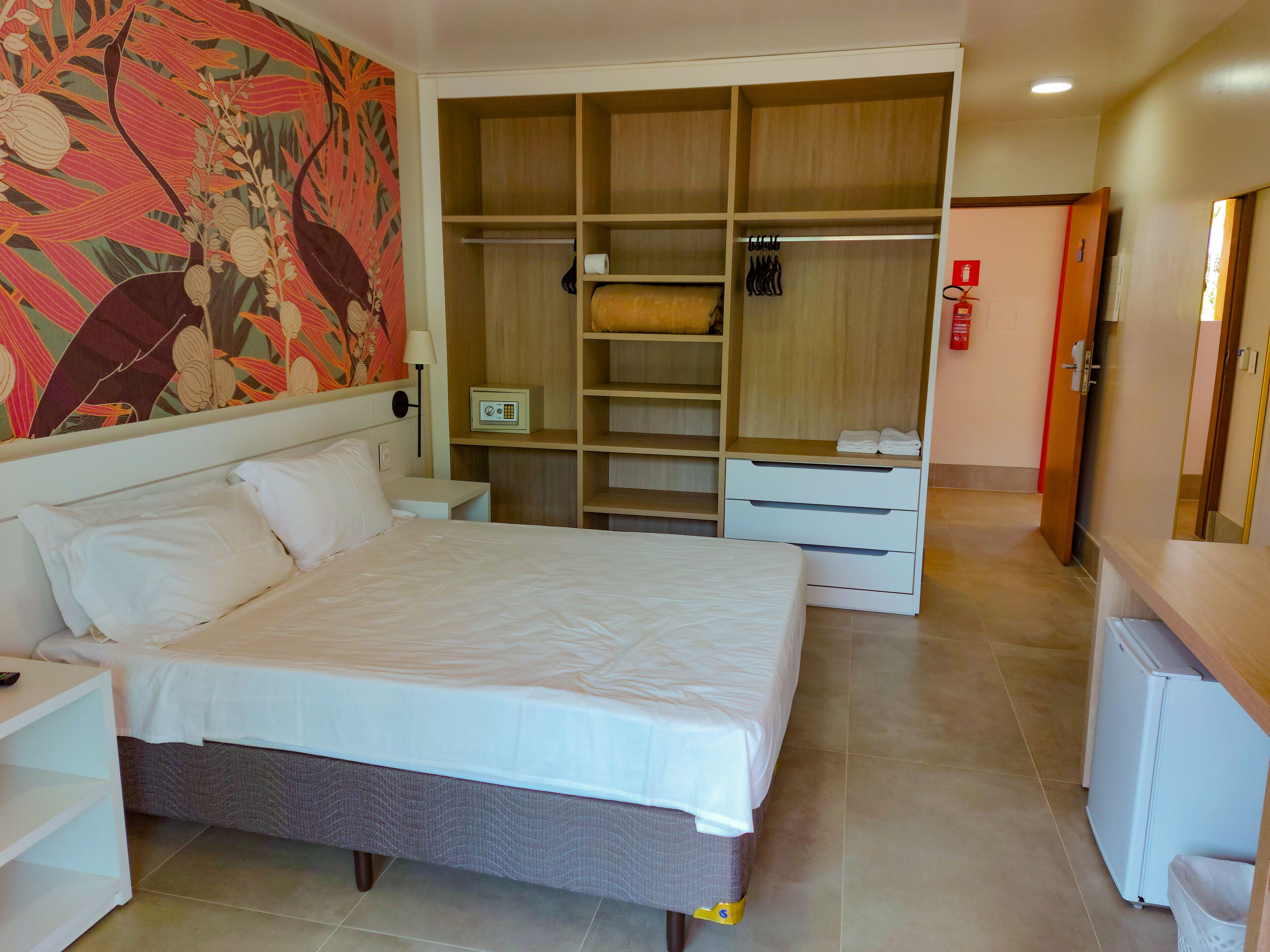 A hotel room with a large bed, a wardrobe with multiple compartments, a small desk, and a wall-mounted lamp.