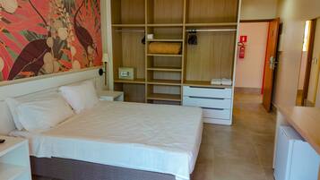 A hotel room with a large bed, a wardrobe with multiple compartments, a small desk, and a wall-mounted lamp.