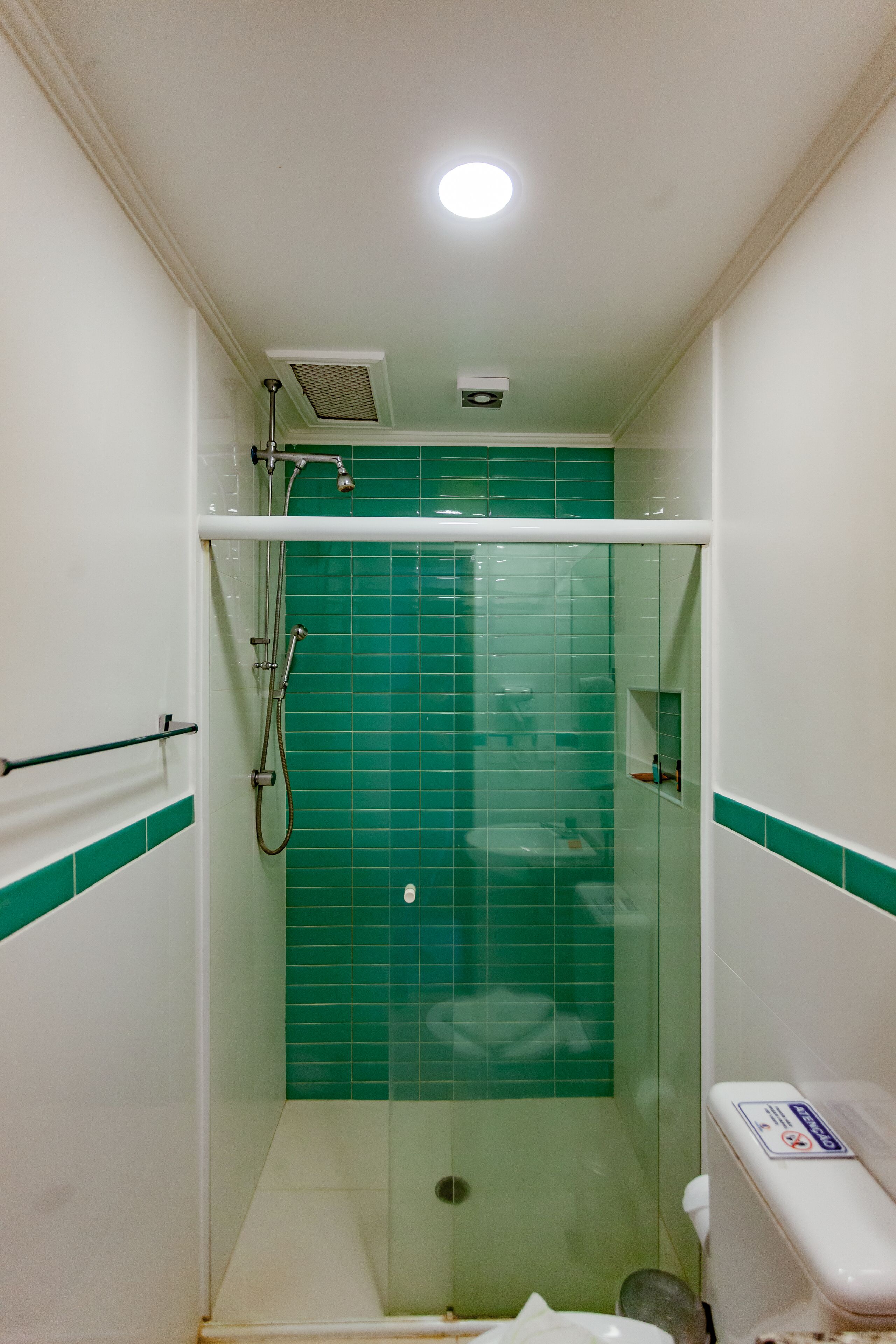 Een kleine, afgesloten douchecabine met groene tegels en een wit toilet.