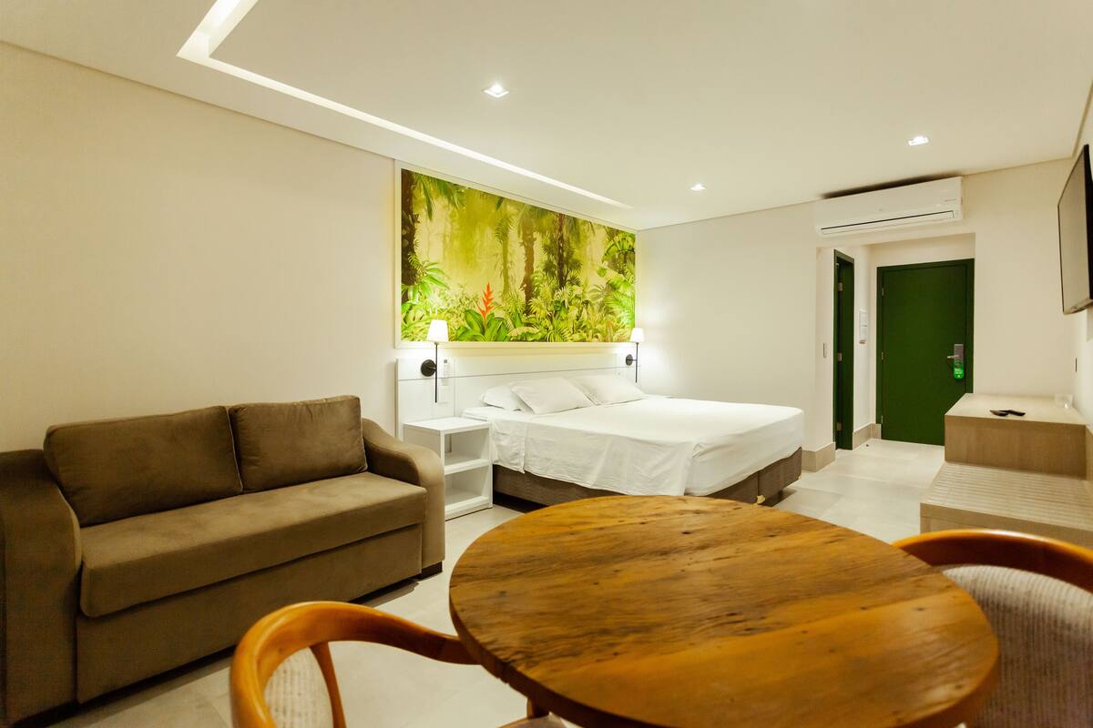 A modern hotel room with a bed, a sofa, a wooden table, and a green door.