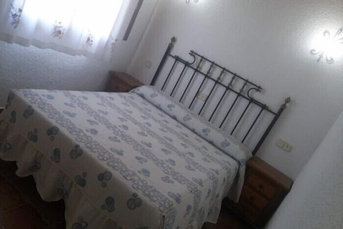 A small, simple room with a bed, a window with curtains, and a plain wall.