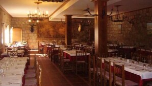 A restaurant with long tables set for dining, stone walls, and chandeliers. - Hotel Casa Rural Ropino (Candeleda)