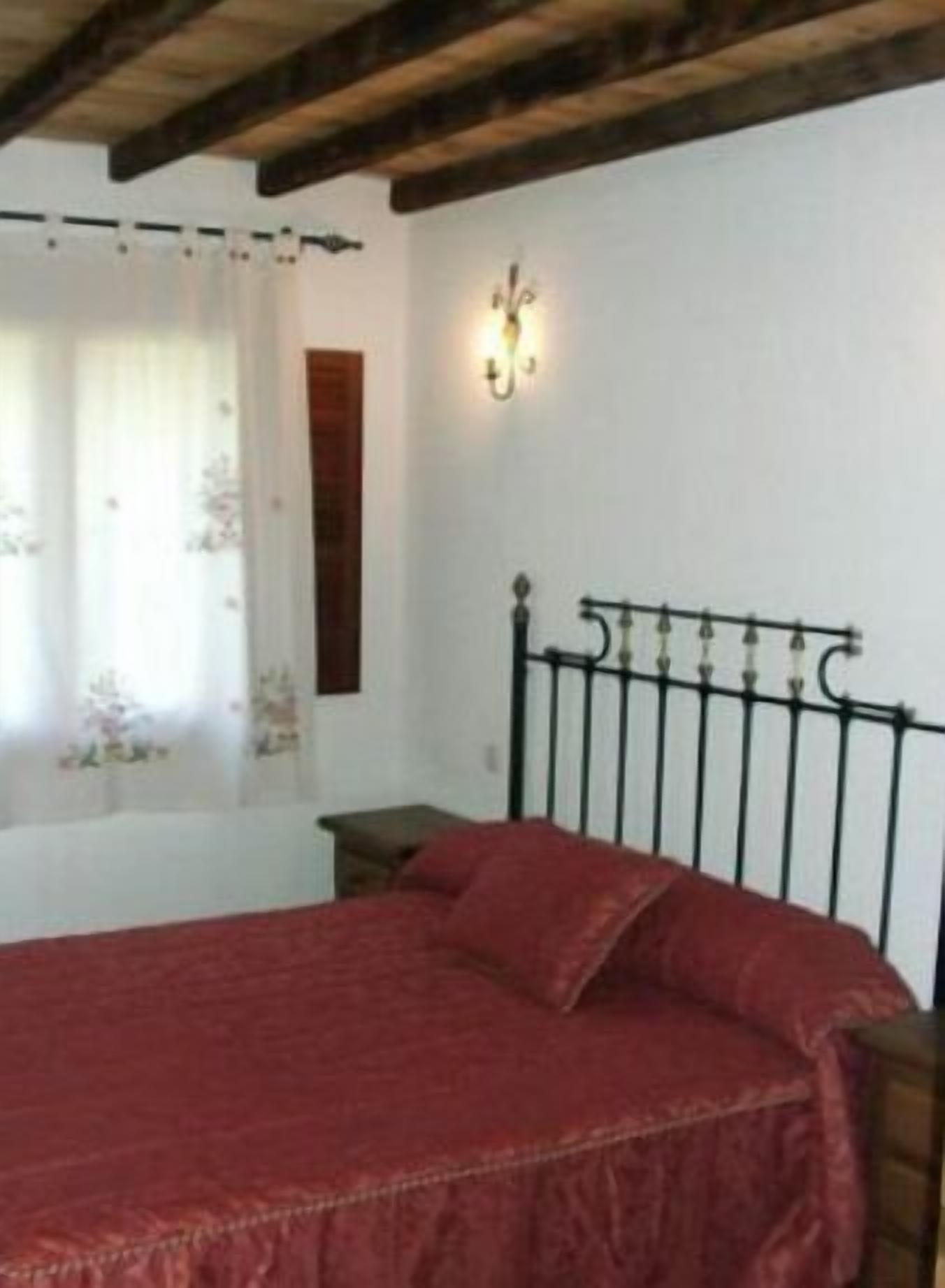 A bedroom with a bed, a nightstand, a wall-mounted lamp, and a window with curtains.