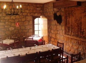 Une salle à manger aux murs de pierre, avec des tables préparées pour deux personnes, un lustre et une tête d’animal empaillée accrochée au mur.