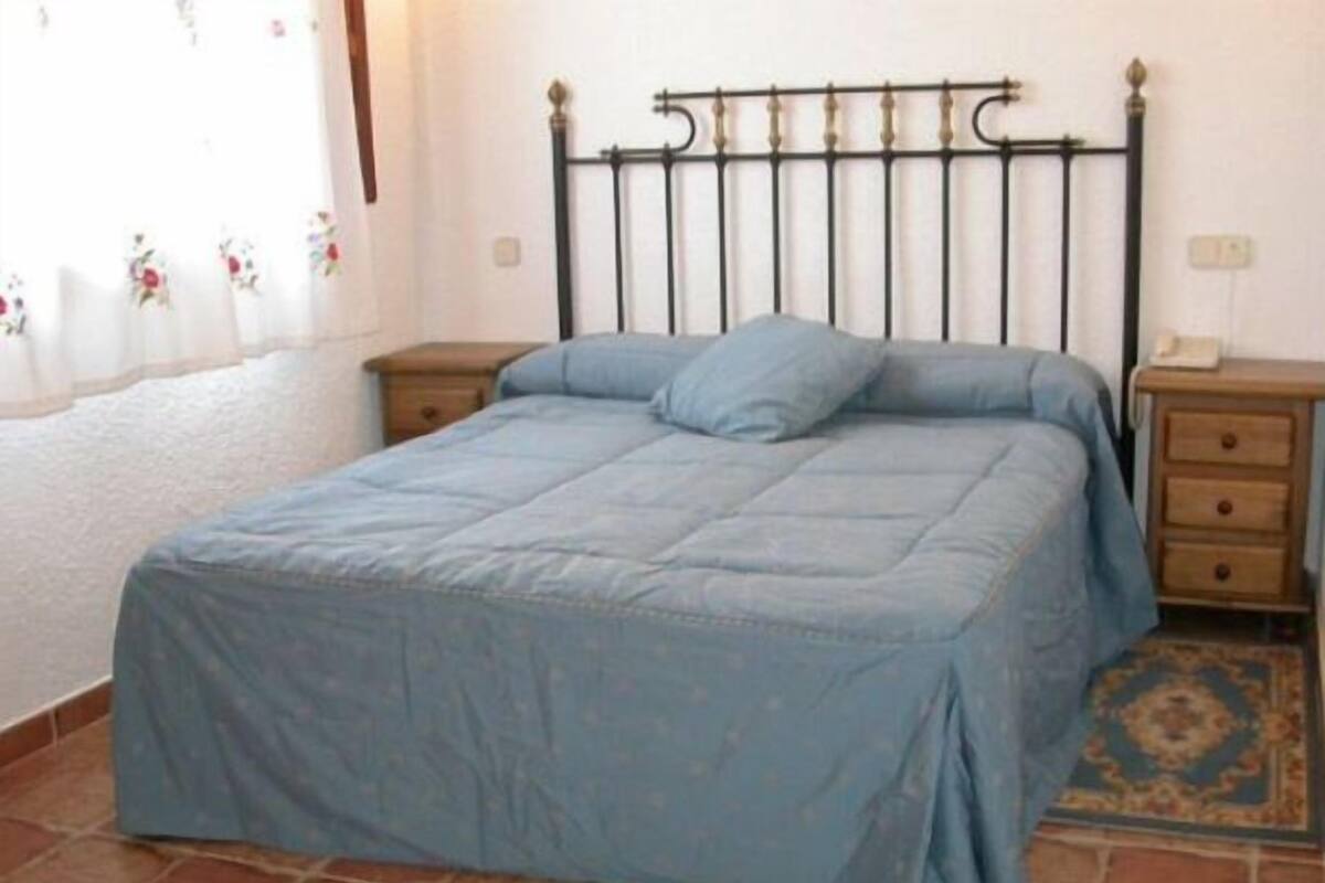 A bedroom with a bed, nightstands, a patterned rug, and a window with curtains.