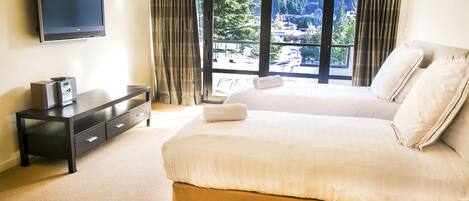 A hotel room with a large bed, a TV, a desk, and a view of mountains through the window.