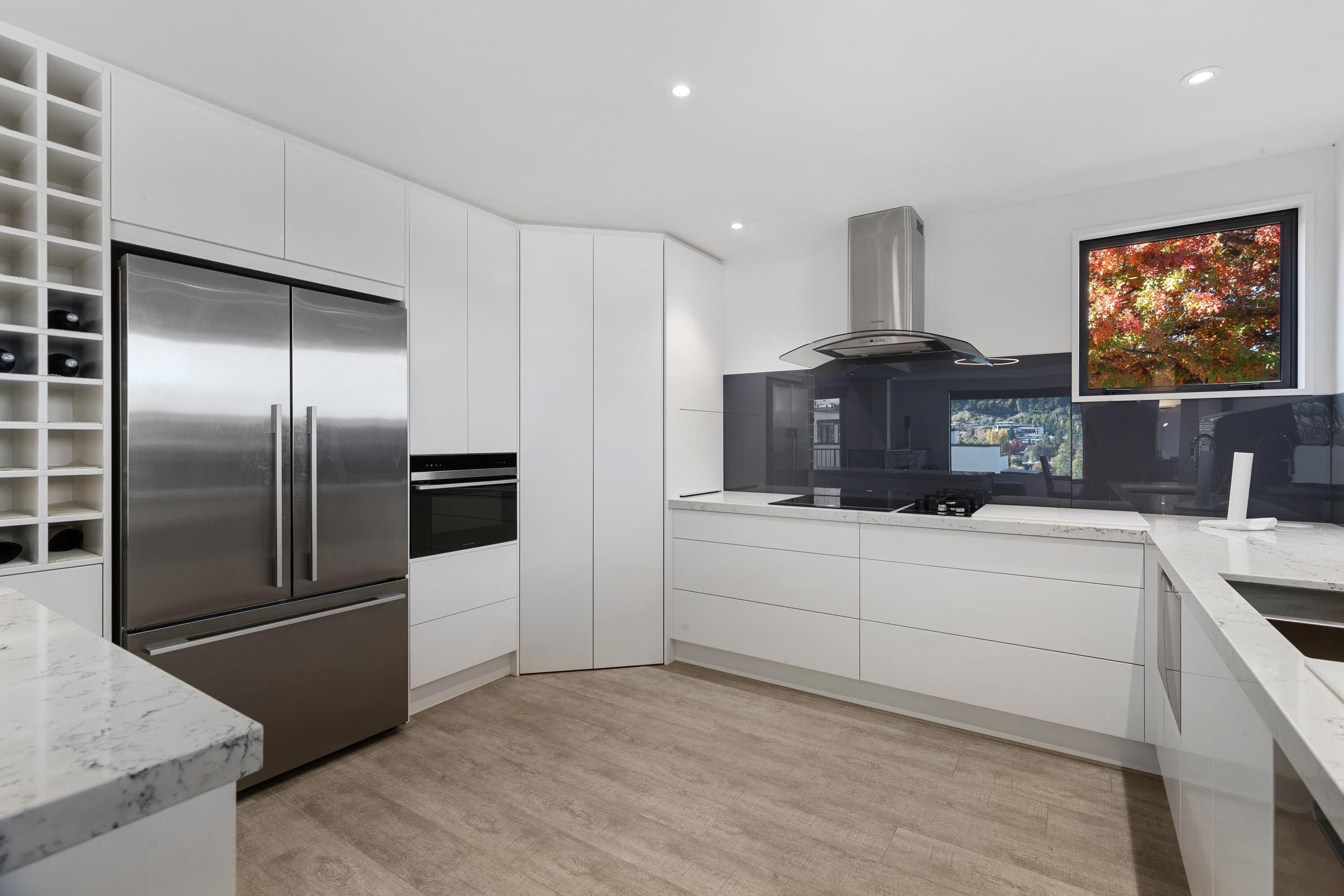 Eine moderne Küche mit weißen Schränken, einem Edelstahlkühlschrank, einem eingebauten Ofen und einem großen Fenster mit Blick auf die Stadt.