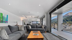 Uma sala de estar moderna com um sofá cinzento, uma mesa de centro de madeira e uma grande janela com vista para as montanhas.