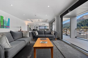 A modern living room with a grey sofa, a wooden coffee table, and a large window offering a mountain view.