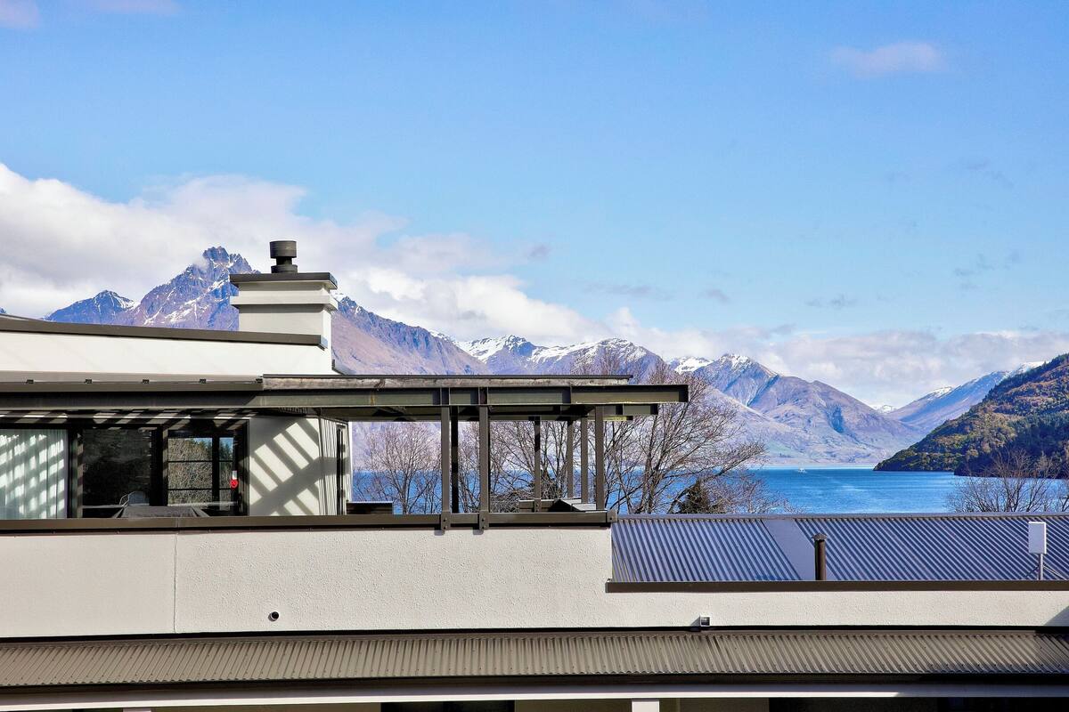 A modern building with a flat roof and large windows overlooking a lake and mountains.