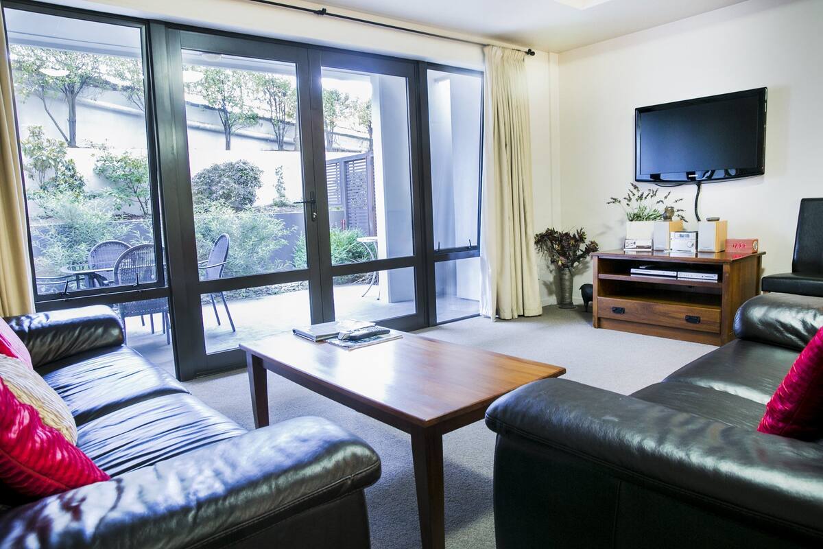 A living room with a sofa, a coffee table, and a TV mounted on the wall.