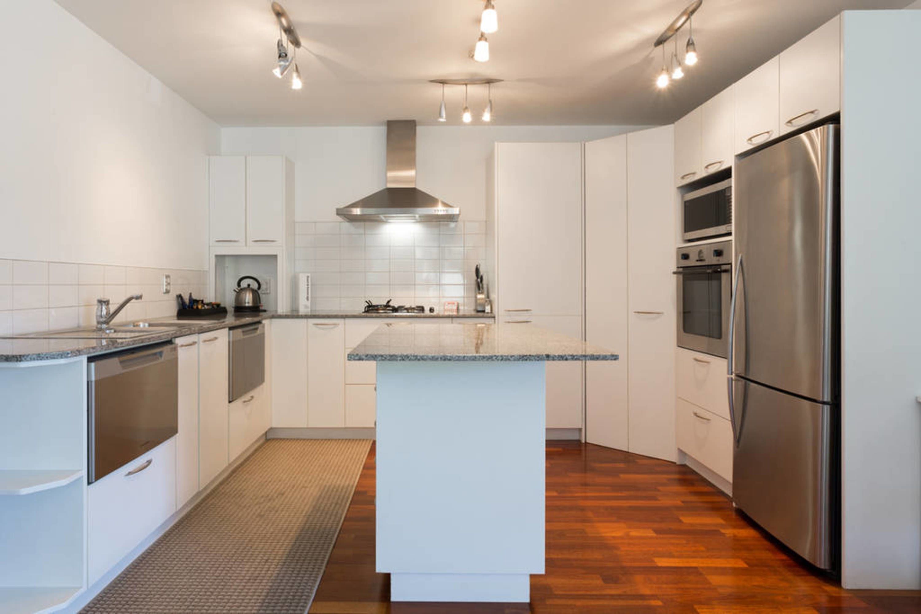 A modern kitchen with white cabinetry, a central island, stainless steel appliances, and a patterned rug.