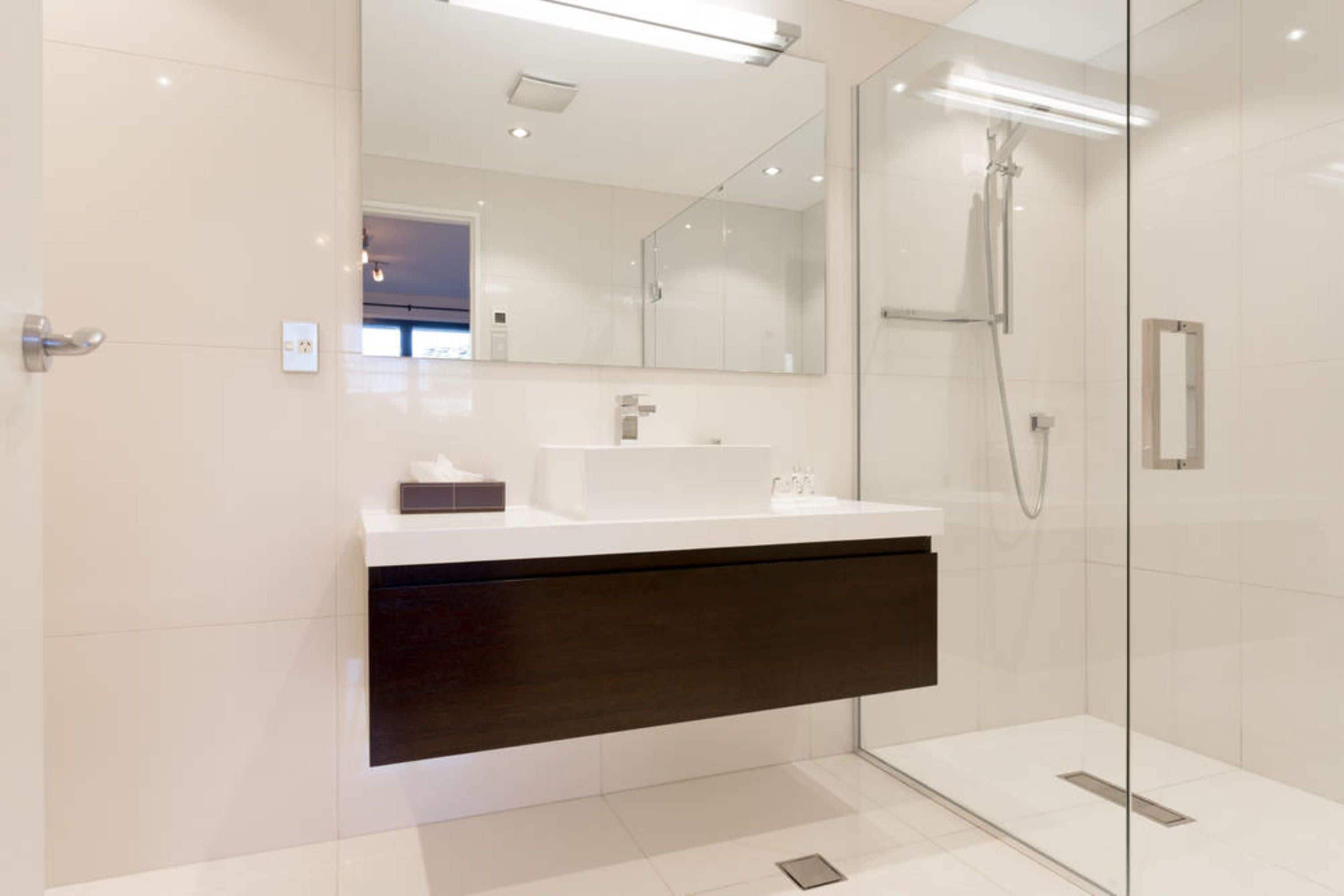 A modern bathroom with a glass shower enclosure, a white vanity with a dark cabinet, and a large mirror above the sink.