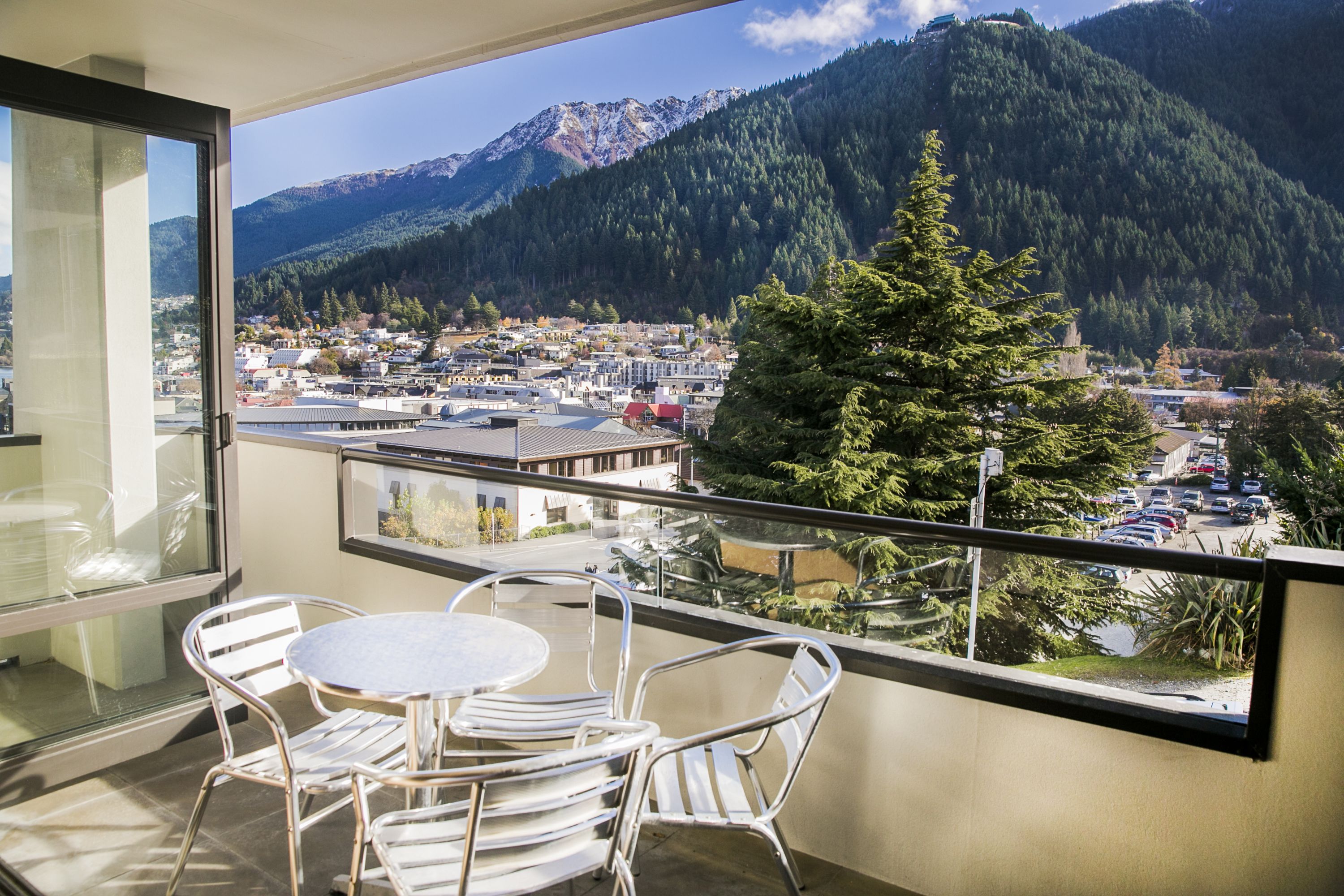 Un balcón con mesa y sillas, con vistas a un pueblo y montañas.