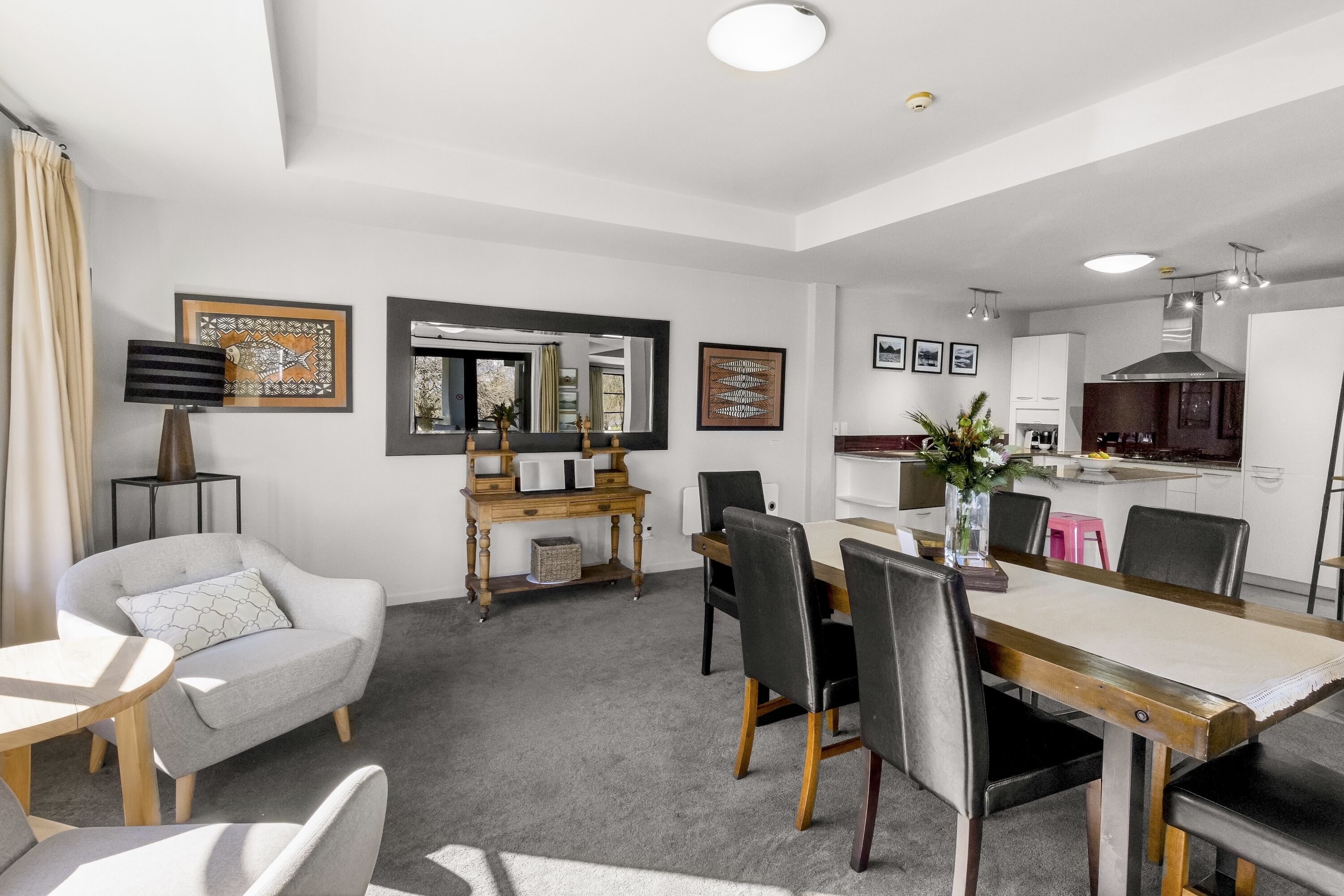 A modern living room with a dining area, a kitchen, and a large mirror.