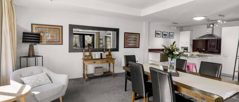 A modern living room with a dining area, a kitchen, and a large mirror.