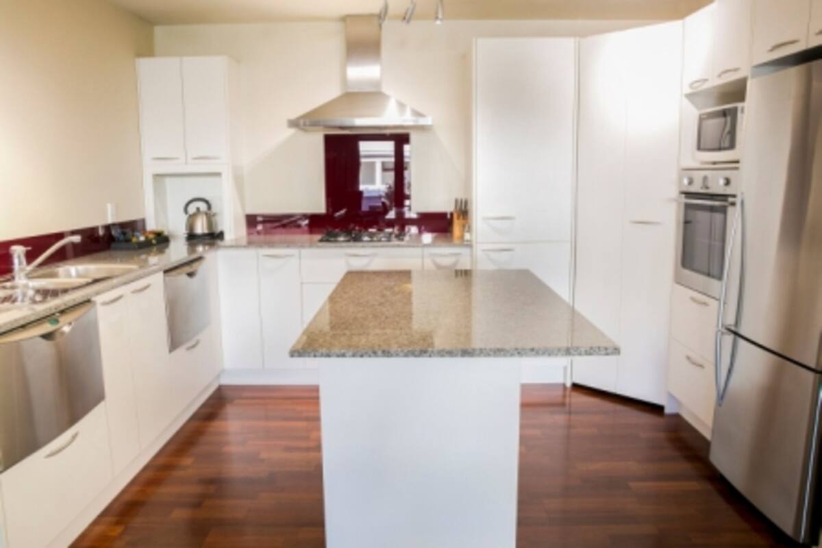 A modern kitchen with white cabinetry, a central island, stainless steel appliances, and a wooden floor.