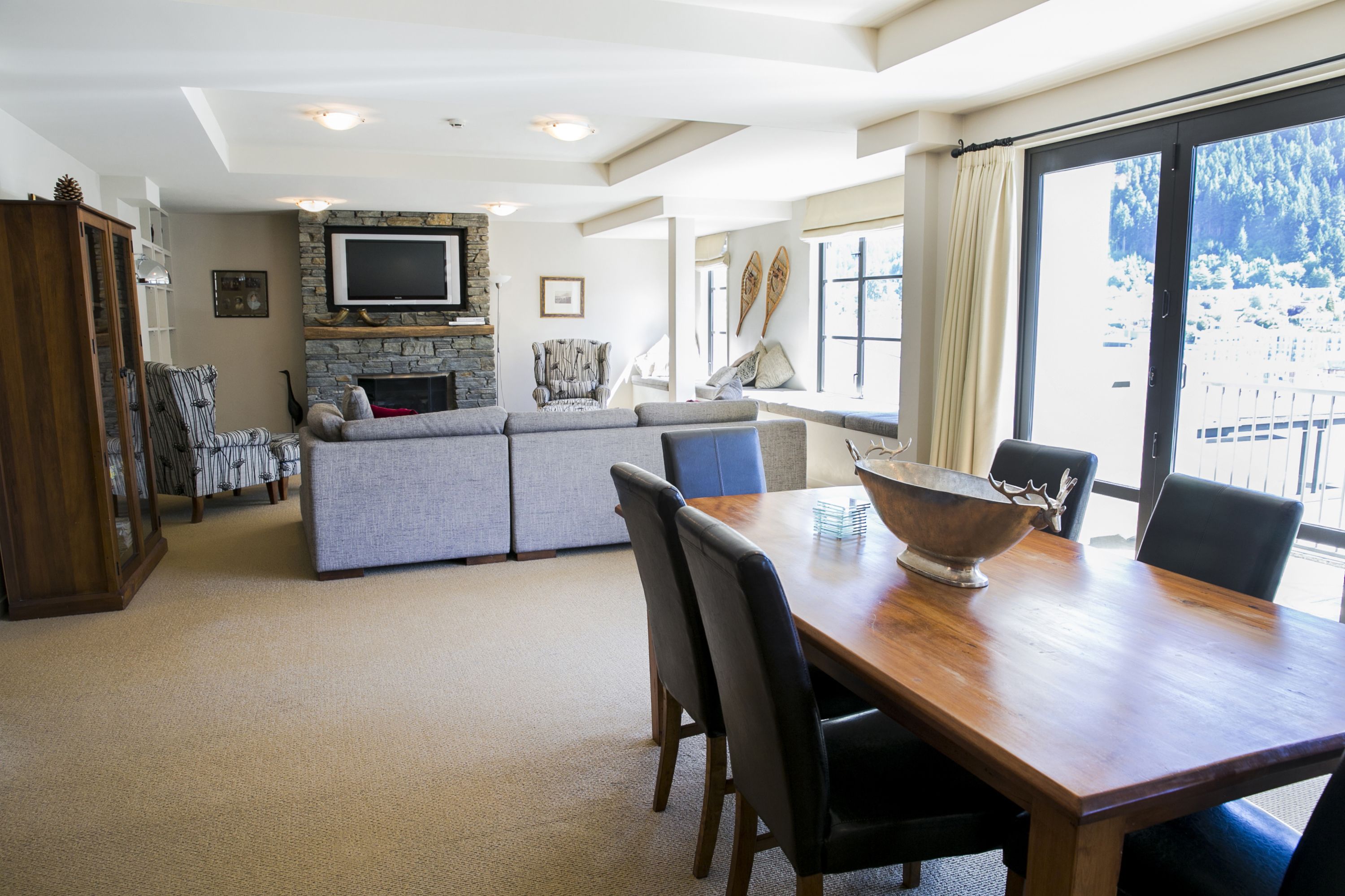 A spacious living area with a fireplace, a dining table, and a large window offering a view of the outdoors.