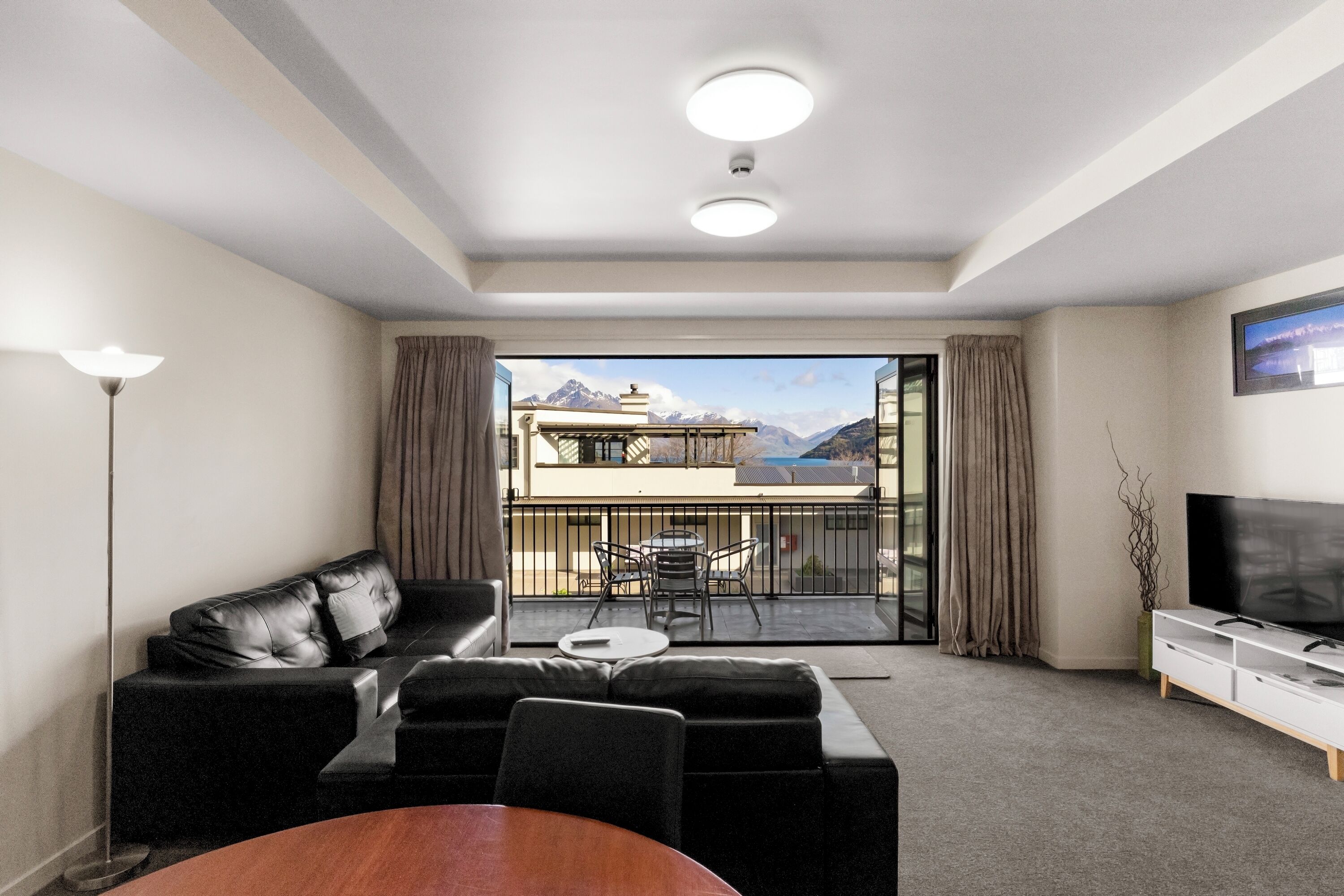 Un salon moderne comprenant un canapé, une table basse et un meuble pour la télévision. Il dispose d’un balcon avec vue sur les montagnes.