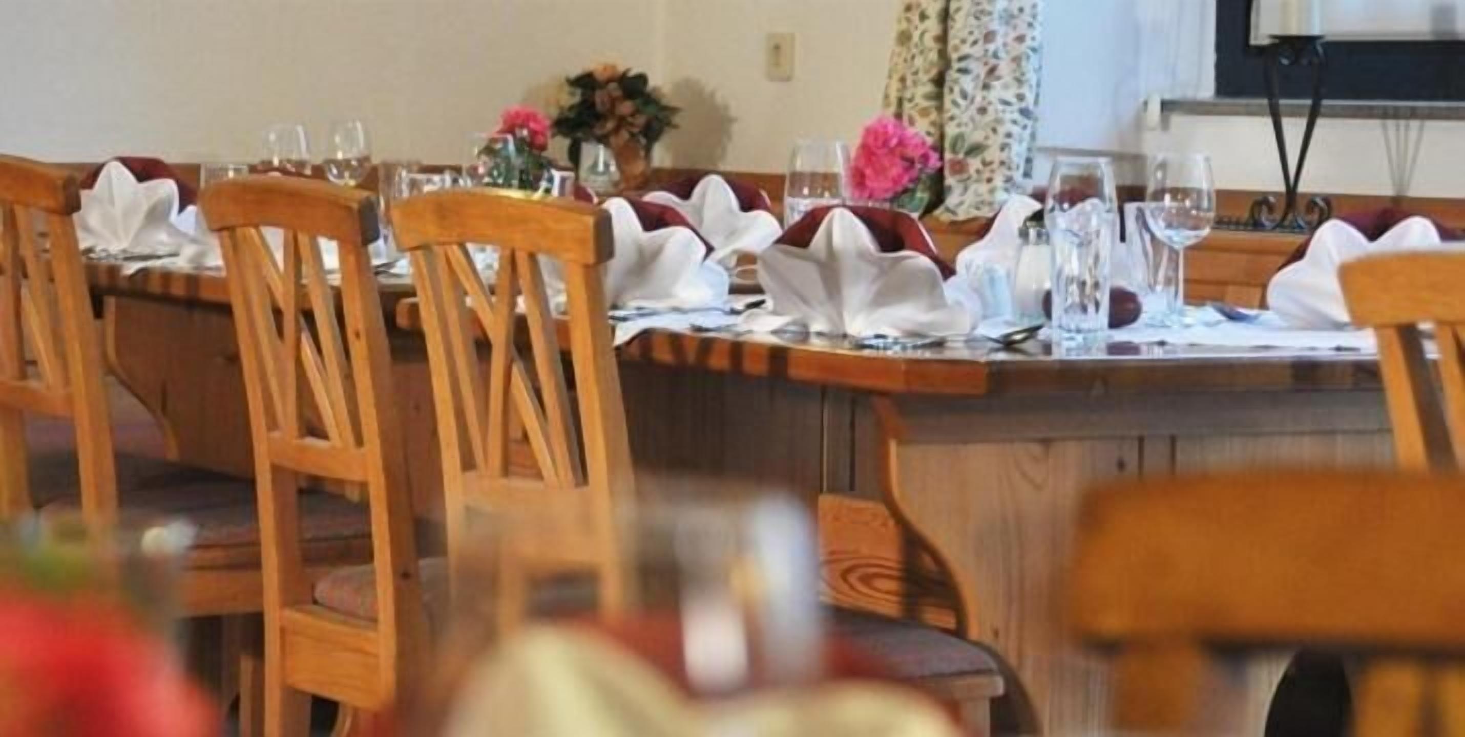 Un comedor con sillas y mesas de madera dispuestas para una comida, con manteles y servilletas blancos.
