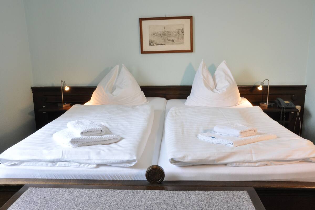 Dos camas ordenadas con sábanas blancas, almohadas y toallas dobladas.