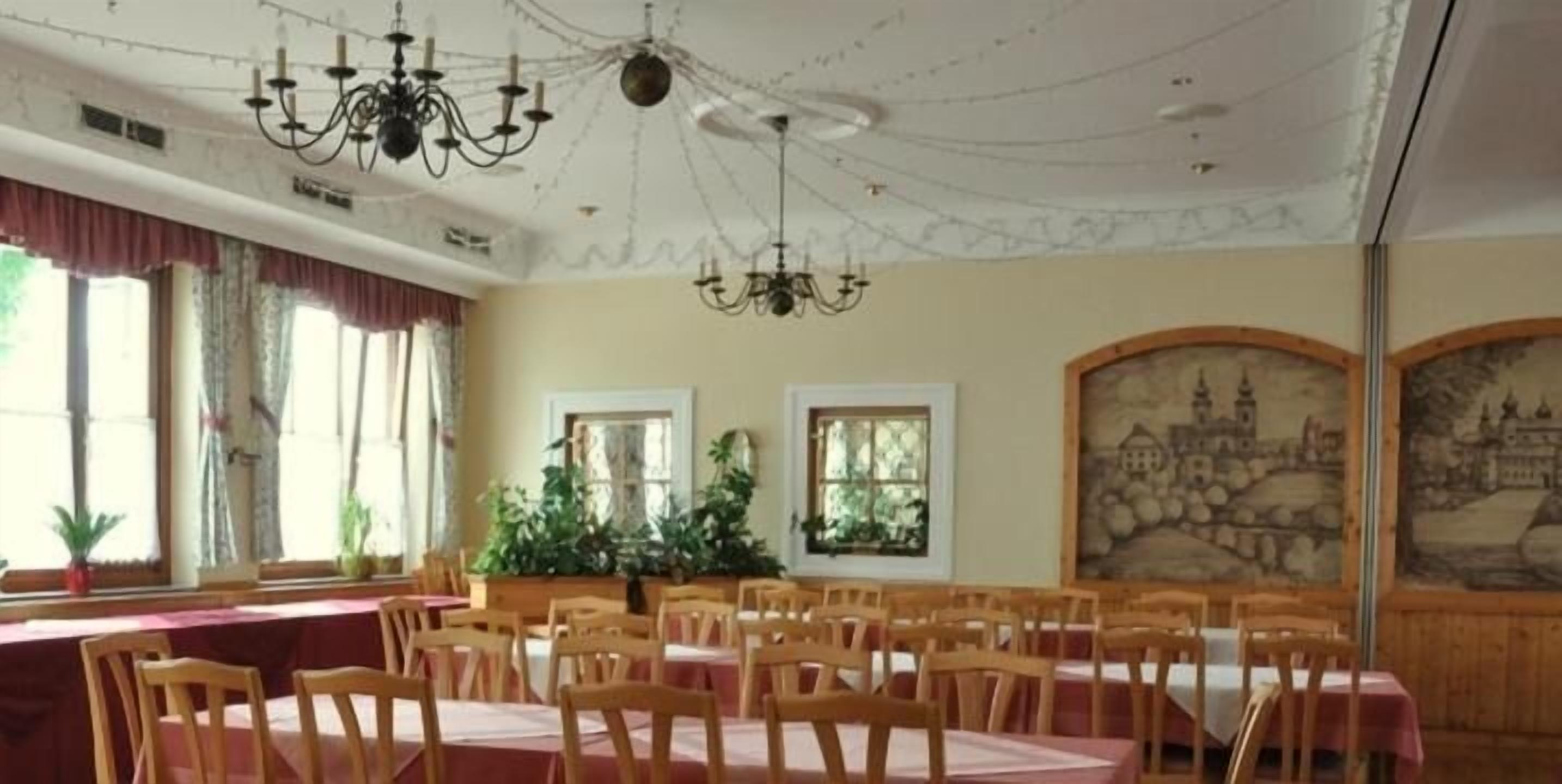 A dining area with multiple tables and chairs, large windows with curtains, and a chandelier.