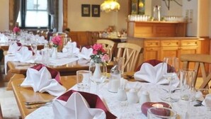 Een eetgedeelte met gedekte tafels, witte tafelkleden, rode servetten en bloemstukken.