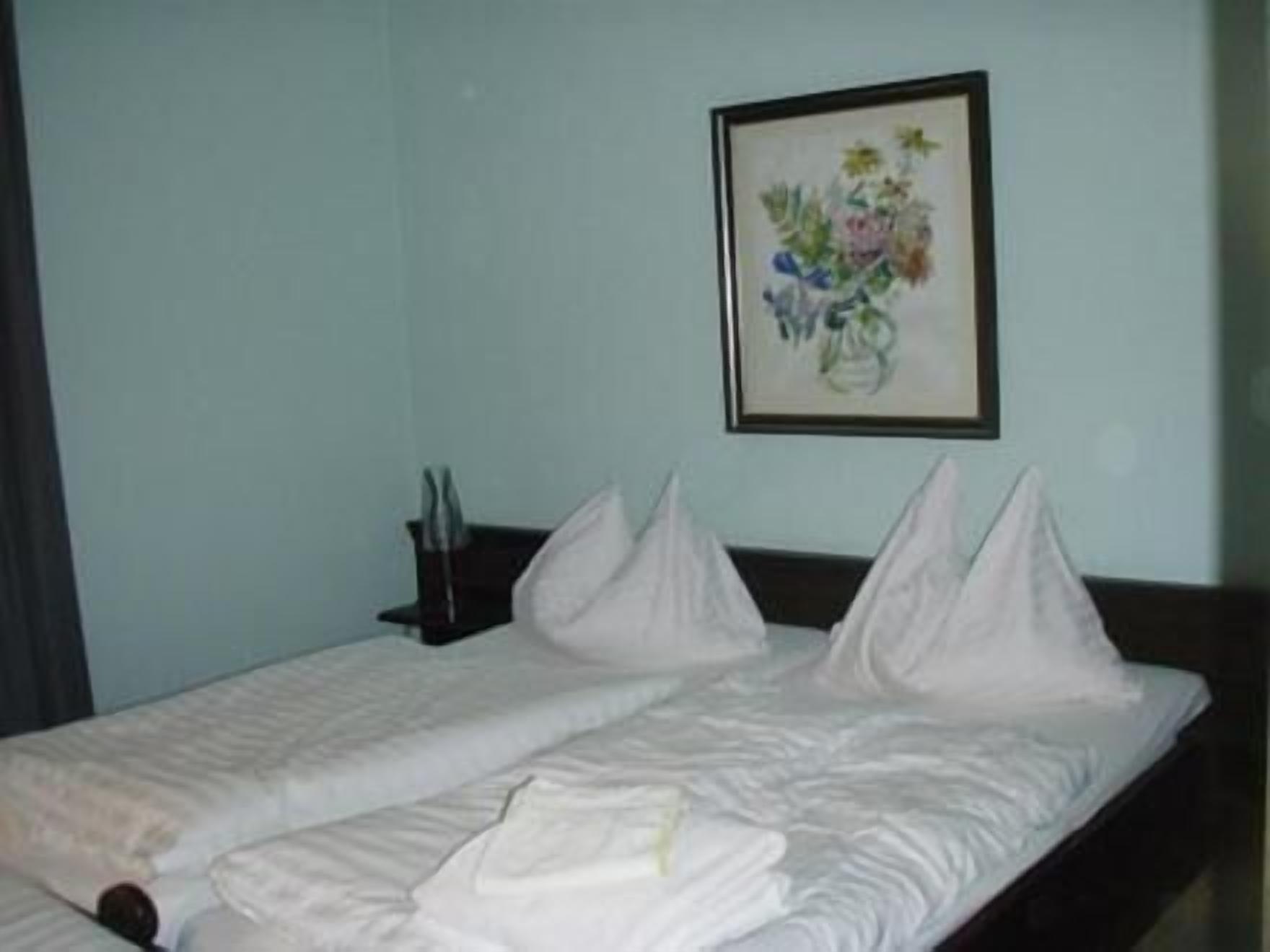 Quarto de hotel com duas camas, uma pintura floral emoldurada na parede e uma mesa de cabeceira com uma xícara e uma colher.
