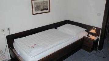 A single bed with a wooden frame, white bedding, and a bedside table with a lamp.