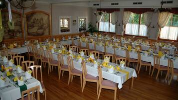 Une grande salle à manger avec de nombreuses tables dressées pour le repas, des chaises en bois et des lustres.