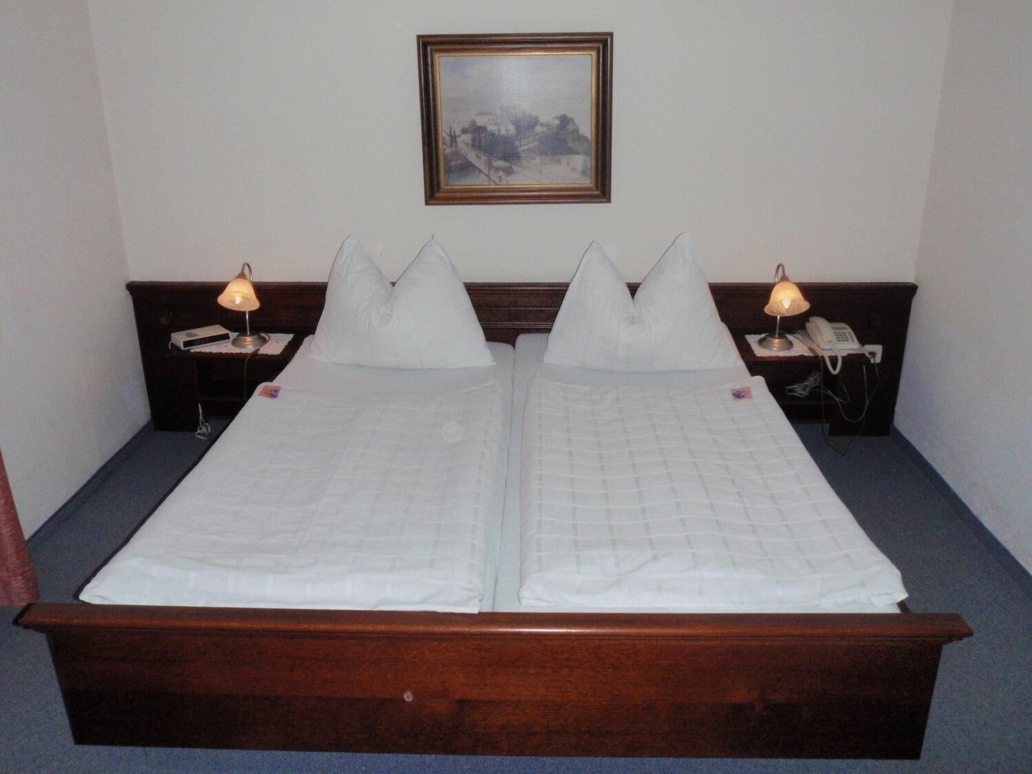 A double bed with two pillows, a wooden headboard, bedside tables with lamps, and a framed picture on the wall.