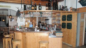 Een houten bar met krukken, flessen en glazen op planken, en krijtbordmenu's.