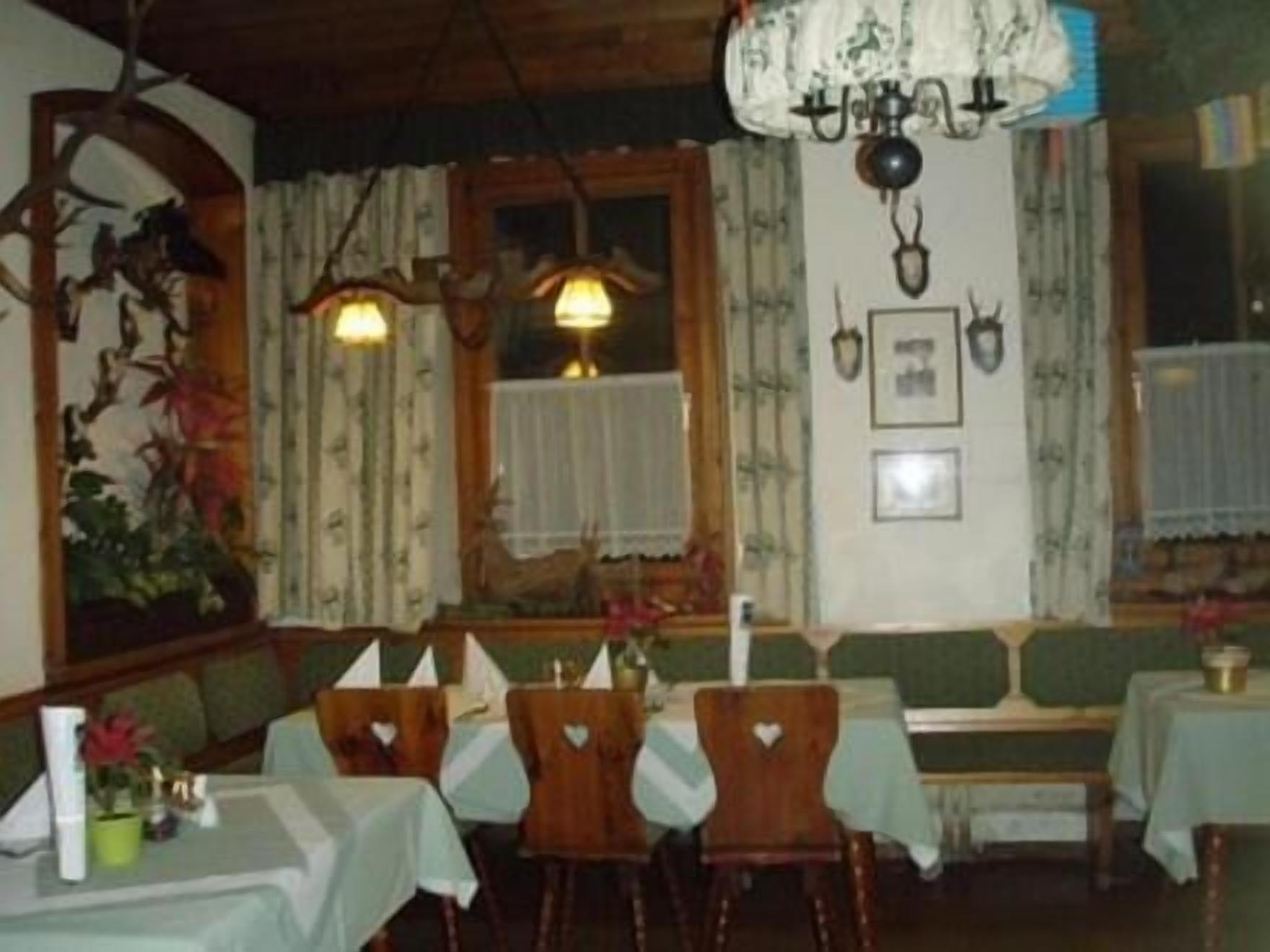 A dining area with wooden tables and chairs, a chandelier, and a wall with framed pictures.