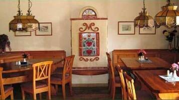 Un comedor con mesas y sillas de madera, un panel decorativo en la pared y lámparas colgantes.