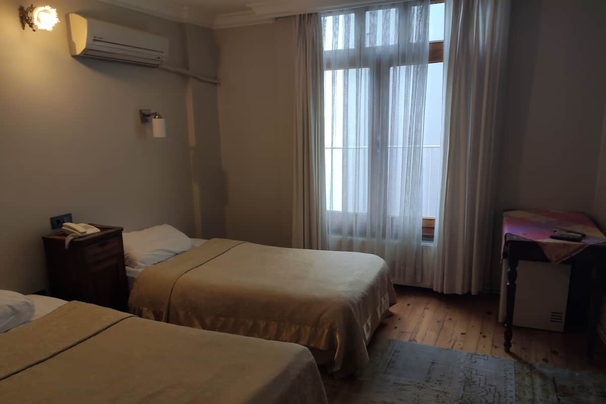 Ein Hotelzimmer mit zwei Betten, einem Schreibtisch, einer Klimaanlage, einem Telefon und einem Fenster mit durchsichtigen Vorhängen.