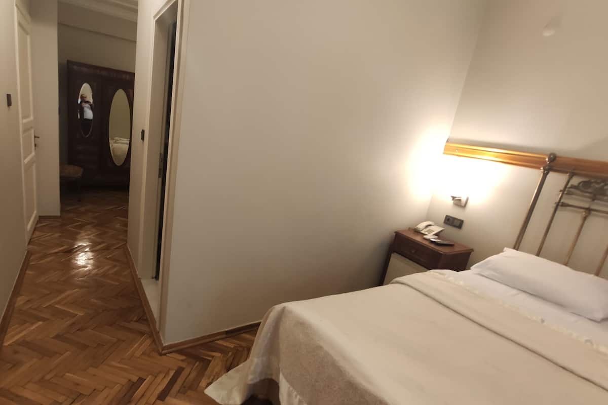 Ein Hotelzimmer mit Holzboden, einem Bett mit weißer Bettwäsche, einem Nachttisch mit Telefon und einem Spiegel an der Tür.