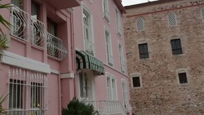 Un edificio rosa con balcones blancos y un edificio de piedra al fondo.