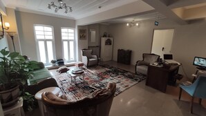 Un salón espacioso con un gran ventanal, un tapete estampado, un sofá verde, una mesa de centro de madera y un escritorio con una computadora.