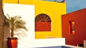 A building with a yellow facade, a pool, and a palm tree.