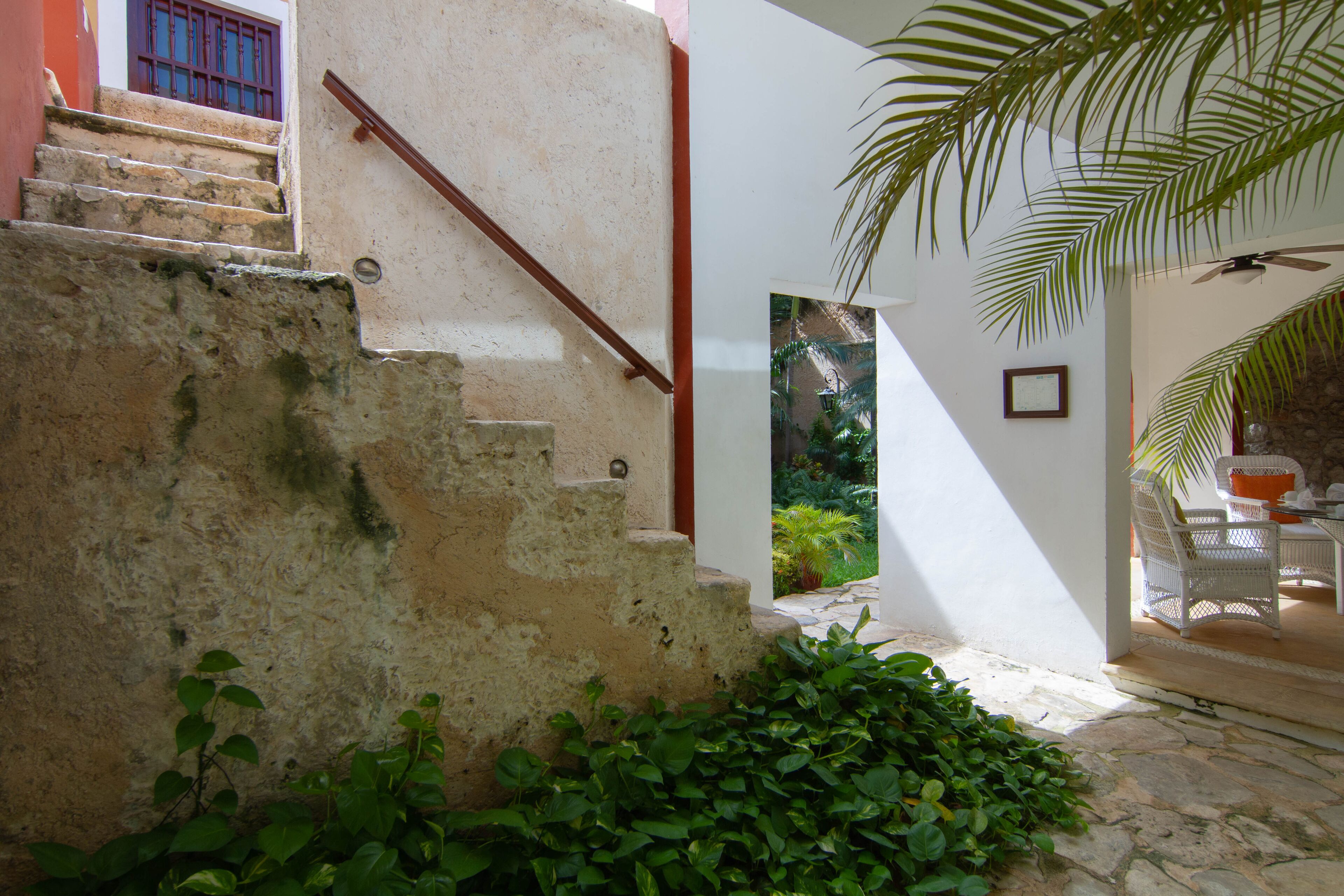 A staircase leading to a covered outdoor area with a ceiling fan, surrounded by greenery.