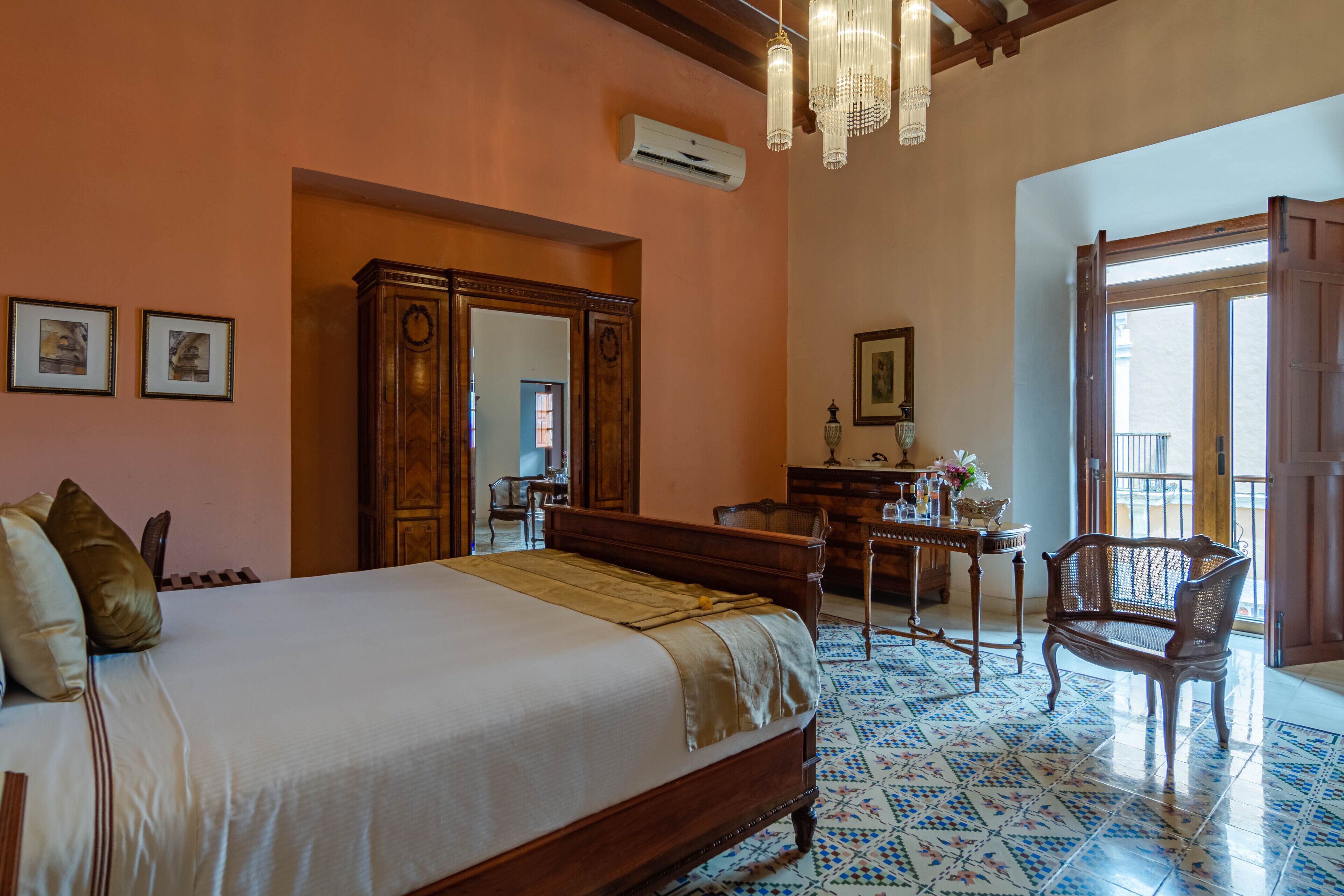 A bedroom with a large bed, wooden wardrobe, a desk with a chair, and a window with a view.