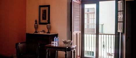 A room with a wooden table, a chair, a patterned rug, a framed picture, and a door leading to a balcony.