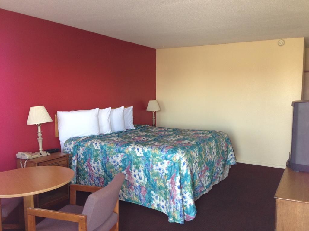 Una habitación de hotel con una cama, dos lámparas de noche, una mesita con una silla y un televisor.