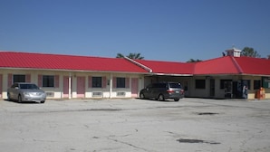 A building with a red roof and a parking lot with two cars. - Super 7 Inn Siloam Springs (Siloam Springs)
