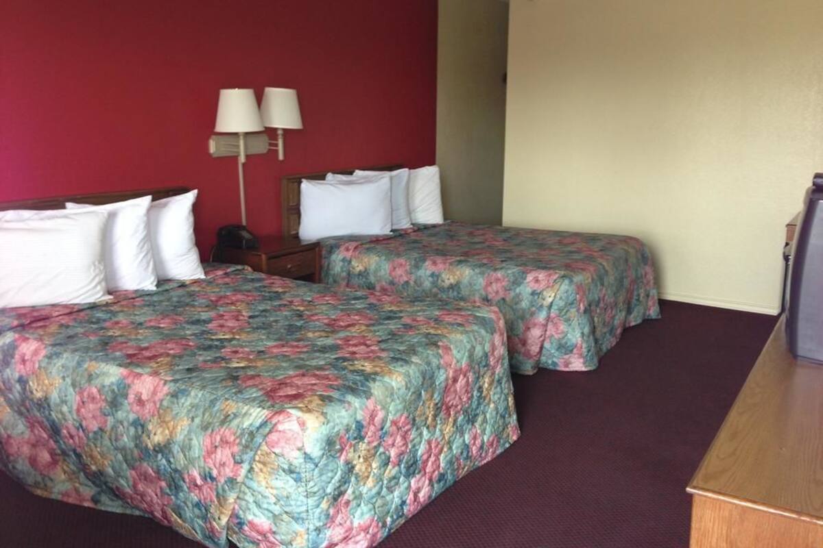 A hotel room with two beds, a desk, and a lamp.