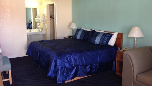 A hotel room with a large bed, two bedside lamps, a wooden nightstand, a chair, and a bathroom visible through an open door. - Super 7 Inn Siloam Springs (Siloam Springs)