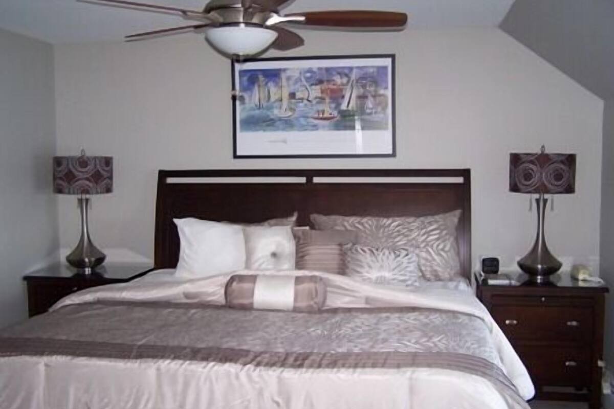 A bedroom with a bed, a ceiling fan, two bedside tables with lamps, and a framed picture on the wall.