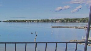 A calm lake with a clear sky, a distant shoreline, and a metal railing in the foreground. - Water Street Inn (Boyne City)