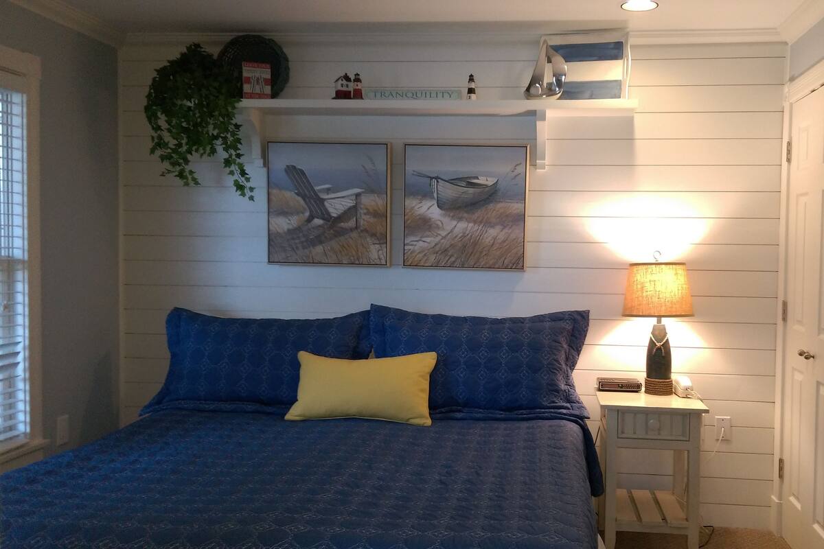 A bedroom with a bed, a nightstand, a lamp, and two wall-mounted paintings.