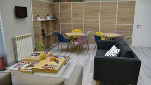 Un salon moderne avec un canapé, une table basse et des fauteuils. Un téléviseur est fixé au mur, et une bibliothèque contient des objets décoratifs.